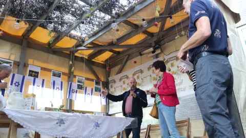 Een gids geeft bezoekers uitleg in de Soeka, met een dak van takken, hangende vruchten en Isra&euml;lische vlaggetjes