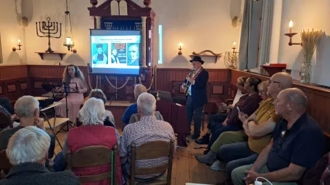 Flip de Liema met gitaar en zangeres Orsaya treden op in de synagoge voor een volle zaal, met beelden op een scherm voor de Heilige Ark