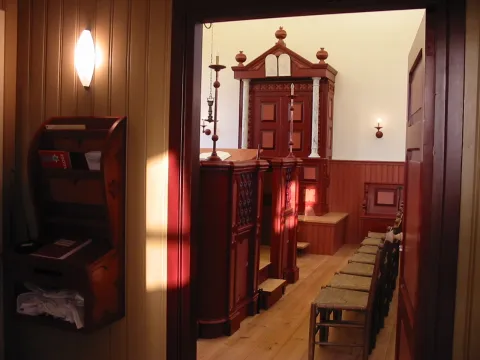 Doorkijk vanuit de hal naar de synagogezaal met de Aron Hakodesj, de bima en een rij biezen stoelen