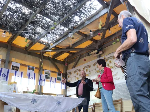 Een gids geeft bezoekers uitleg in de Soeka, met een dak van takken, hangende vruchten en Isra&euml;lische vlaggetjes