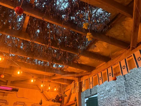 Het dak van de Soeka, bedekt met takken en behangen met vruchten en lichtjes, naast de bakstenen muur van de synagoge