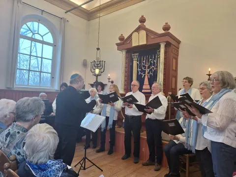 Het koor Al Naharot zingt onder leiding van de dirigent in de Dijksynagoge, met publiek op de voorgrond